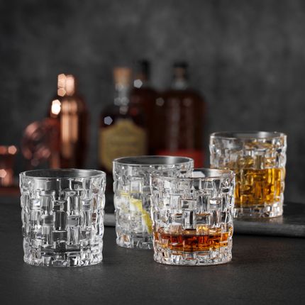 Vier NACHTMANN Bossa Nova SOF-Gläser, drei davon entweder mit Whiskey oder anderen Getränken gefüllt, eines davon leer. Im Hintergrund stehen Schnapsflaschen.<br/>