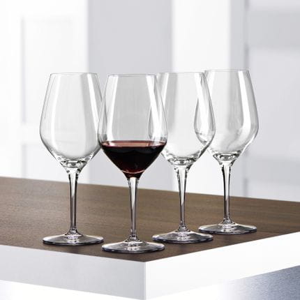 Four SPIEGELAU Authentis Red Wine glasses on a table, one of them is filled with red wine.<br/>