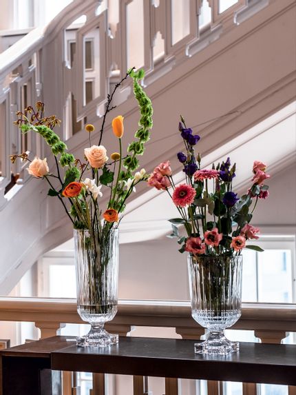 The Nachtmann Minerva Tall is on the left and the Nachtmann Minerva Small is on the right, both filled with flowers. Both sit on a tabletop next to a staircase.