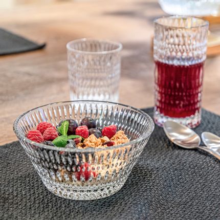 The NACHTMANN Ethno bowl filled with cereals and berries on a table mat. In the background are a with juice filled Ethno longdrink glass and an empty tumbler. On the right of the table are two spoons.<br/>