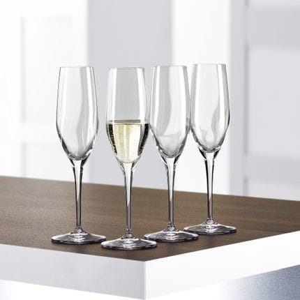 Vier SPIEGELAU Authentis Champagnerflöten auf einem Tisch, eine davon ist mit Sekt gefüllt.<br/>