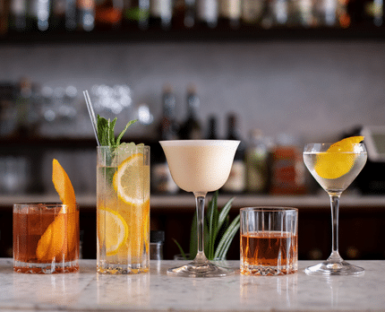 RIEDEL Drinks Specific Glassware collection lined up on a bench filled with mixed cocktails.