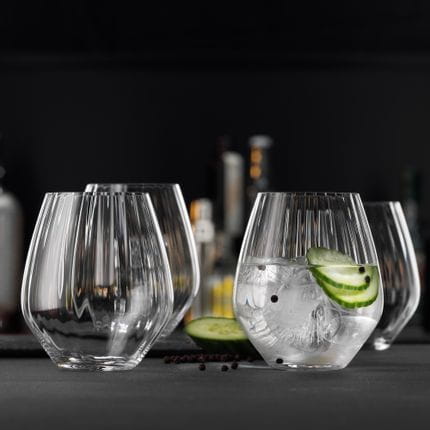 Quatre gobelets SPIEGELAU Gin and Tonic avec des effets de lignes optiques dans le design du verre sur une table. L'un des verres est rempli d'un cocktail Gin-Tonic au concombre et au poivre noir.<br/>