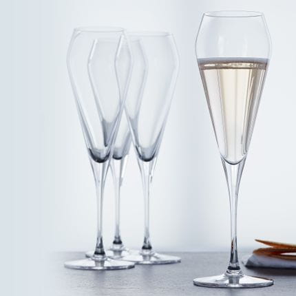 Four SPIEGELAU Willsberger Anniversary Champagne glasses, one of them filled with Champagne.<br/>