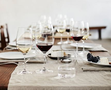 RIEDEL Vinum filled on table setting with white linen cloth.