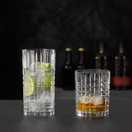 Das NACHTMANN Highland Square Longdrinkglas gefüllt mit einem klaren Drink mit Limette und Eiswürfeln und der Tumbler gefüllt mit Whiskey auf Eis.<br/>