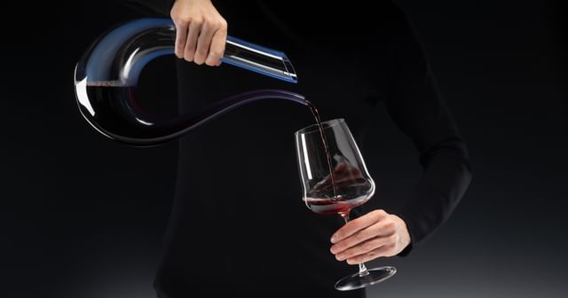 hands pouring wine from a decanter into a glass