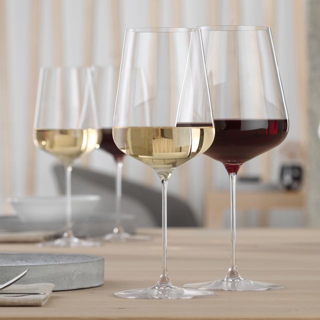Un verre à bordeaux SPIEGELAU Definition rempli de vin rouge et un verre à vin blanc SPIEGELAU Definition rempli de vin blanc sur une table.