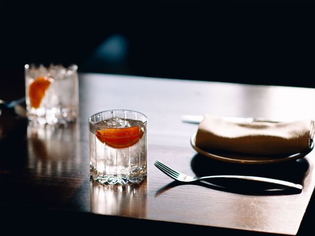 Two RIEDEL Drink Specific Glassware Rocks glasses filled with G&T on a restaurant wooden table.