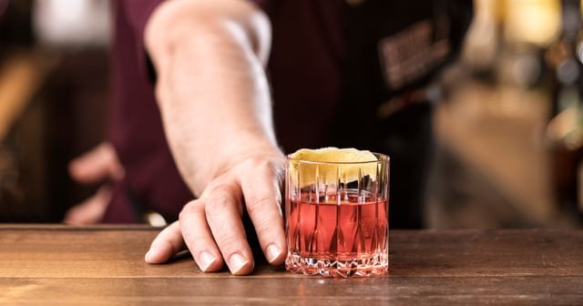 neat glass filled with a cocktail garnished with a zest, the bartender pushes the glass to the guest