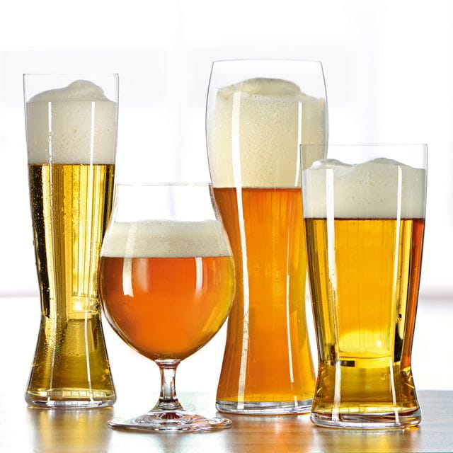 I quattro bicchieri SPIEGELAU Beer Classics in fila, pilsner, beer tulip, bicchiere da birra di frumento e lager. Riempiti con varie birre, si trovano su un tavolo di legno con uno sfondo chiaro.<br/>
