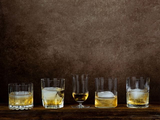 RIEDEL Whisky glasses in a row on brown backdrop.