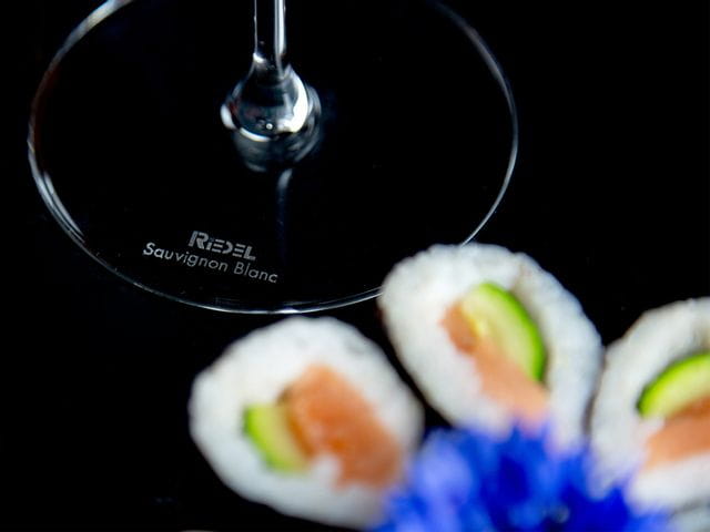 The base of a RIEDEL glass with the varietal Sauvignon Blanc engraved next to sushi.