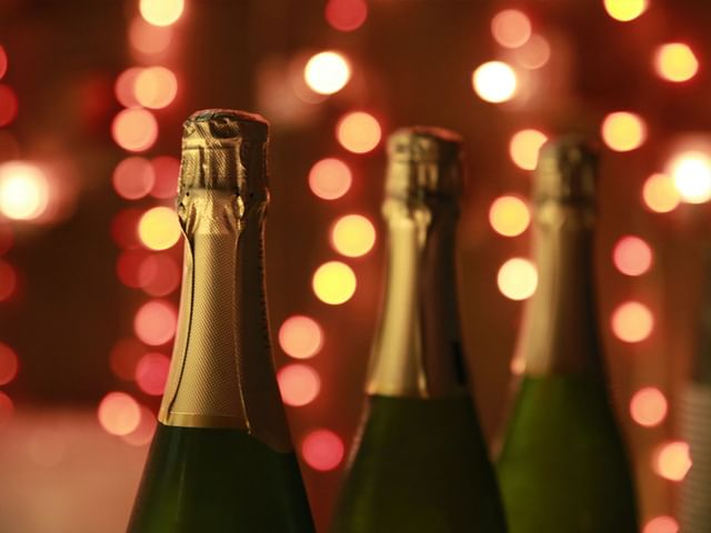 The top of three Champagne bottles with fairy lights in the background.