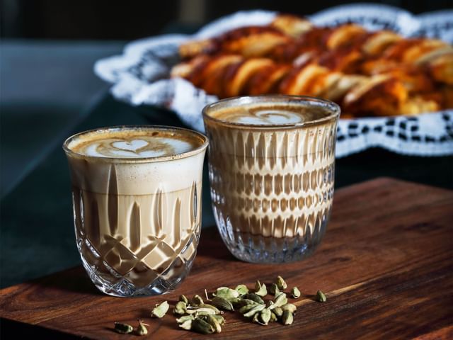 The NACHTMANN Barista Ethno and Noblesse Cappuccino/Flat White glass filled with coffee with pastries in the backdrop.
