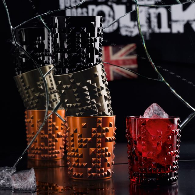 Four NACHTMANN Punk tumblers in jet-black, copper and gun metal stacked up in front of a broken mirror. Besides them the Punk tumbler in ruby filled with ice cubes. In the mirror there is a Junion Jack and the line nextgen goes punk.<br/>