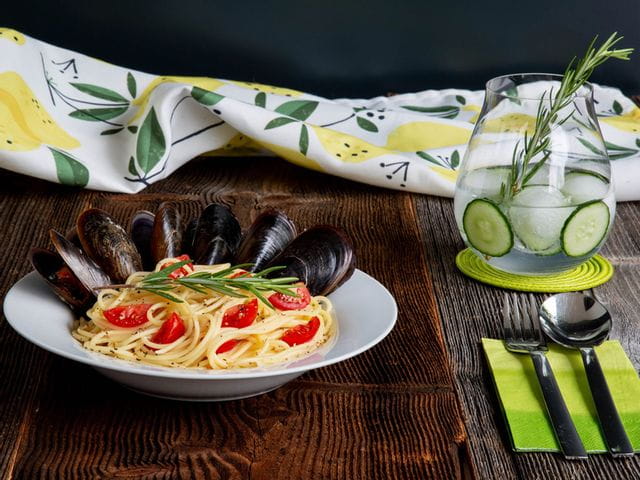RIEDEL Gin Set Classic glass filled with gin & tonic on a table top next to a bowl of gin & lemon pasta with mussels.