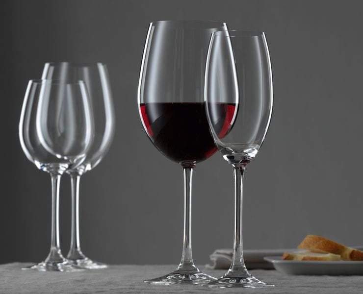 Le verre NACHTMANN Vivendi Bordeaux rempli de vin rouge et la flûte à champagne vide sur une table recouverte d'une nappe.<br/>